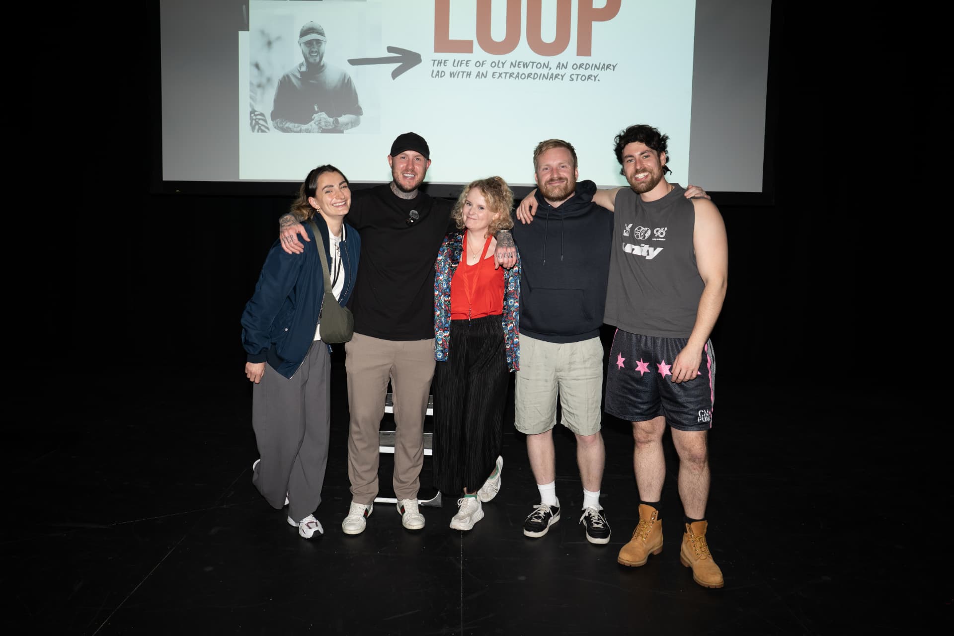 Oly Newton with the LOOP cast and crew on stage at Leeds Playhouse in front of the LOOP title slide