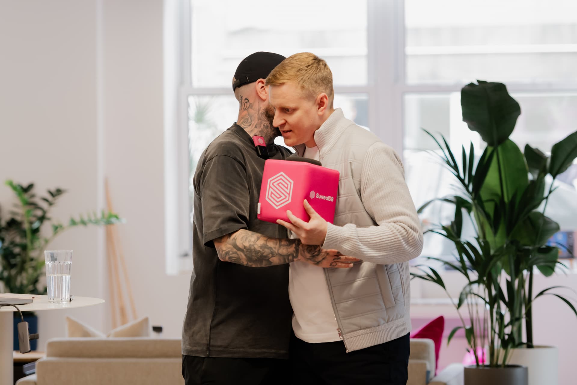 Oly Newton hugging an organiser on stage after a talk, both holding a pink microphone cube between them