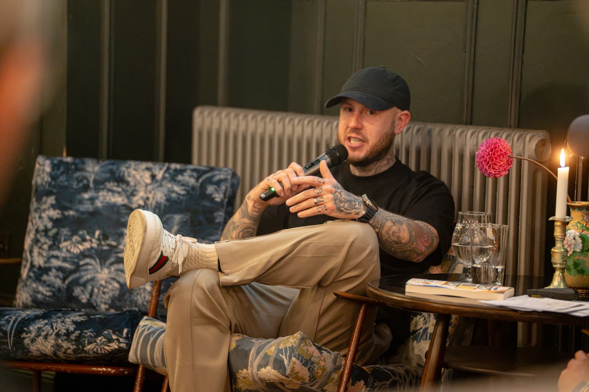 Oly Newton speaking at his book launch, seated in an armchair with a microphone